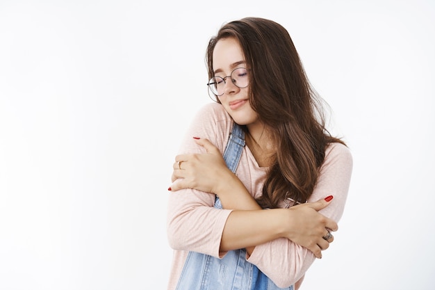 Mulher romântica, sonhadora e bonita, abraçando-se com os olhos fechados, encostada no ombro e sentindo-se nostálgica