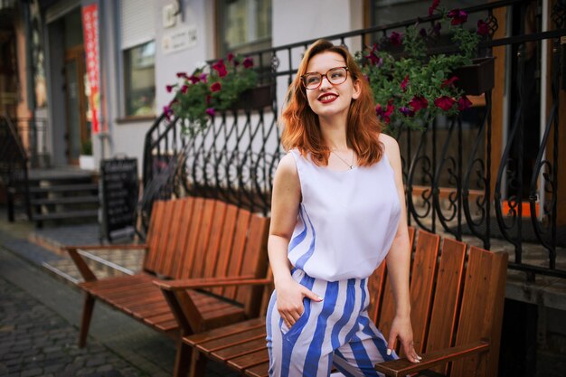 Mulher ruiva atraente de óculos posando na rua da cidade de primavera