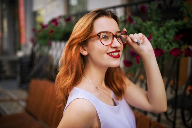 Mulher ruiva atraente de óculos posando na rua da cidade de primavera