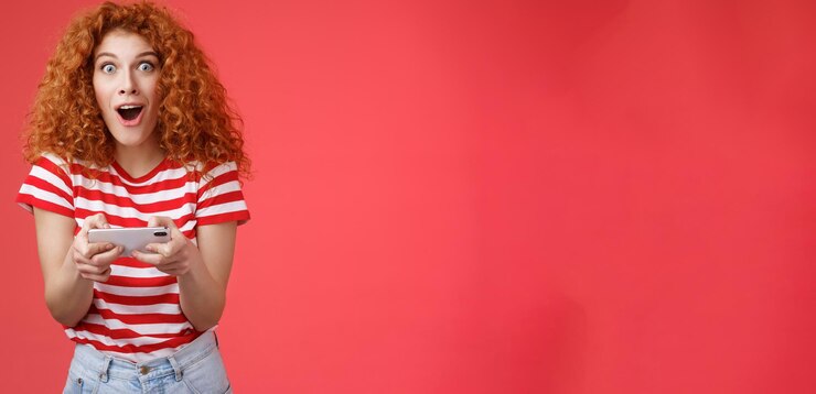 Foto grátis mulher ruiva bonita e animada impressionada segura smartphone boca aberta horizontalmente fascinada s