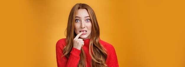 Mulher ruiva bonita e boba fazendo expressão inocente, segurando o dedo no lábio e parecendo assustada wi