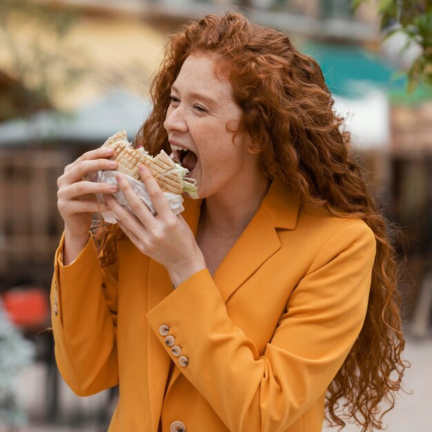 Mulher ruiva comendo comida de rua