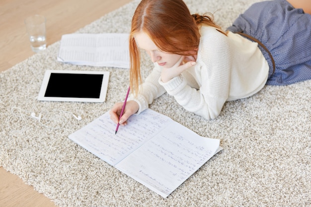 Mulher ruiva deitada no chão com notebook e tablet