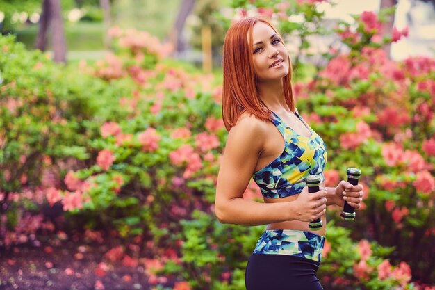 Mulher ruiva desportiva relaxante no parque de verão ao ar livre.