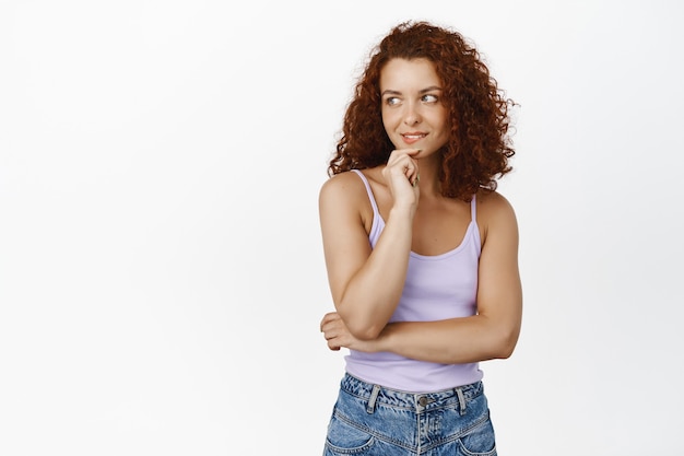 Mulher ruiva elegante e pensativa, olha e pondera, com expressão facial coquete à esquerda, pensando, tentada a experimentar algo em branco