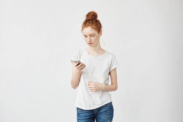 mulher ruiva em fones de ouvido, olhando para o telefone.