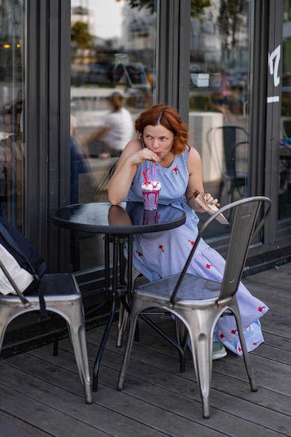 Mulher ruiva em um café bebe um coquetel de verão, feliz, ri, sorri.