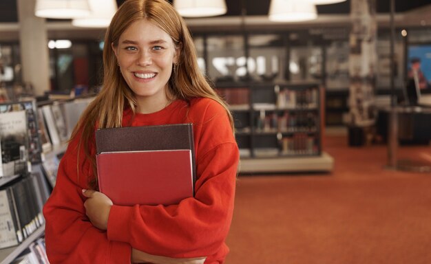 mulher ruiva estudando, segurando livros na livraria e sorrindo.