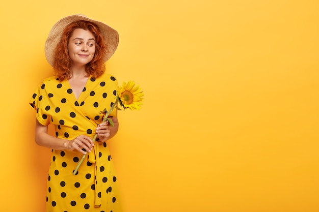 Foto grátis mulher ruiva linda posando com vestido polca amarelo e chapéu de palha