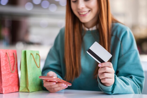 Mulher ruiva segurando o telefone e cartão de crédito