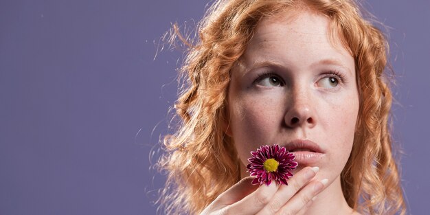 Mulher ruiva segurando uma flor perto da boca com espaço de cópia