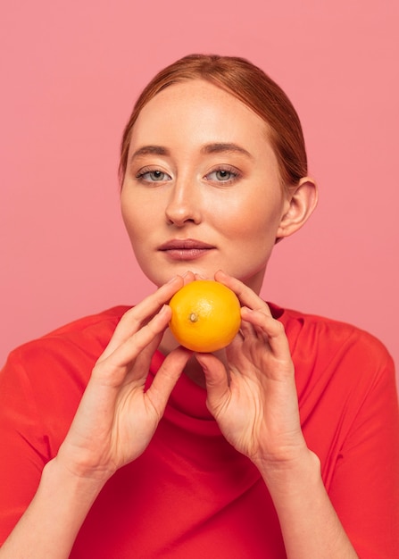 Mulher ruiva segurando uma laranja