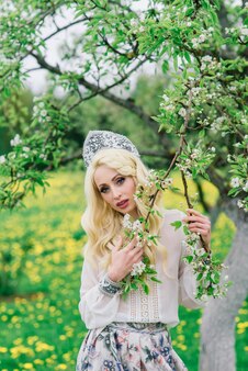 Mulher russa elegante em vestido folclórico nacional tradicional, cocar eslavo, flores brancas de primavera.