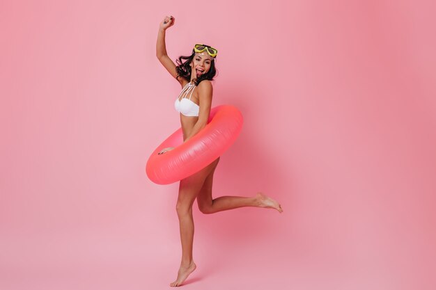 Mulher satisfeita de biquíni pulando no fundo rosa
