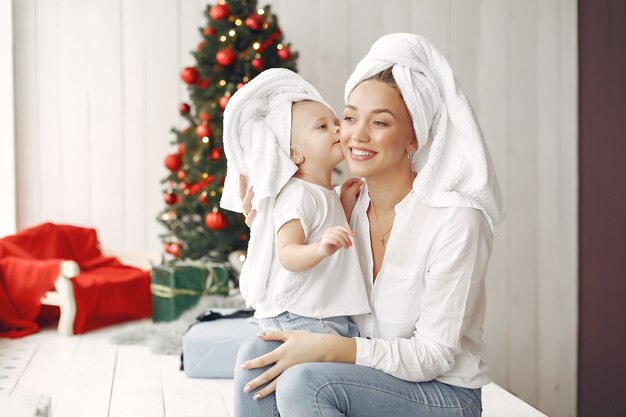 Mulher se diverte se preparando para o Natal. Mãe em uma camisa branca está brincando com sua filha. Família está descansando em uma sala festiva.