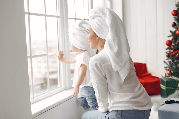 Mulher se diverte se preparando para o natal. mãe em uma camisa branca está brincando com sua filha. família está descansando em uma sala festiva.