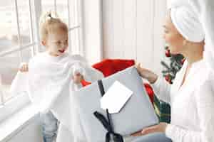 Foto grátis mulher se diverte se preparando para o natal. mãe em uma camisa branca está brincando com sua filha. família está descansando em uma sala festiva.