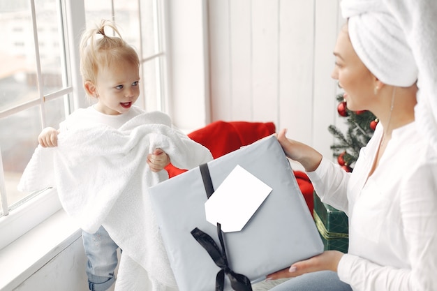 Mulher se diverte se preparando para o Natal. Mãe em uma camisa branca está brincando com sua filha. Família está descansando em uma sala festiva.