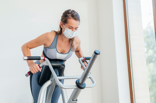 Mulher se exercitando na academia com máscara e equipamento