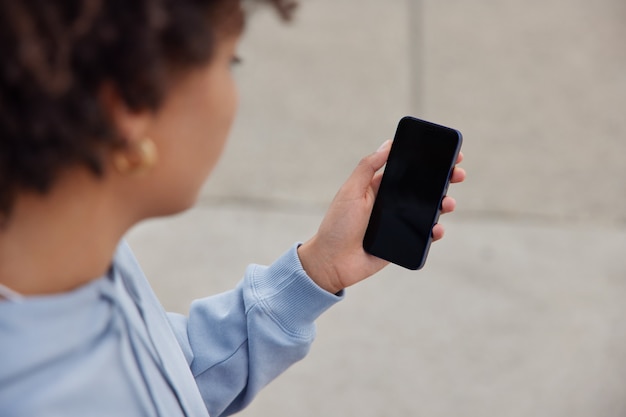 mulher segura telefone celular com tela de espaço de cópia para sua mensagem de texto ou conteúdo de informação usa aplicativo de celular para compras online usa moletom poses ao ar livre