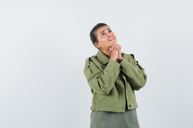 mulher segurando as mãos entrelaçadas na jaqueta, camiseta e parecendo um sonho.