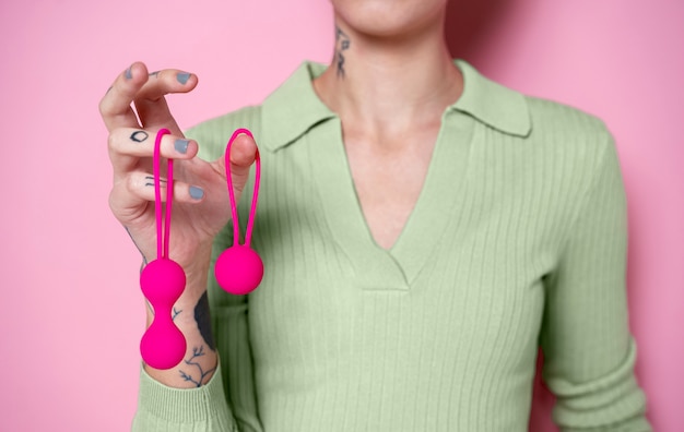 Mulher segurando brinquedos sexuais com fundo rosa