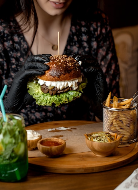 Mulher segurando com luvas pretas, hambúrguer de carne com cogumelos, alface e queijo