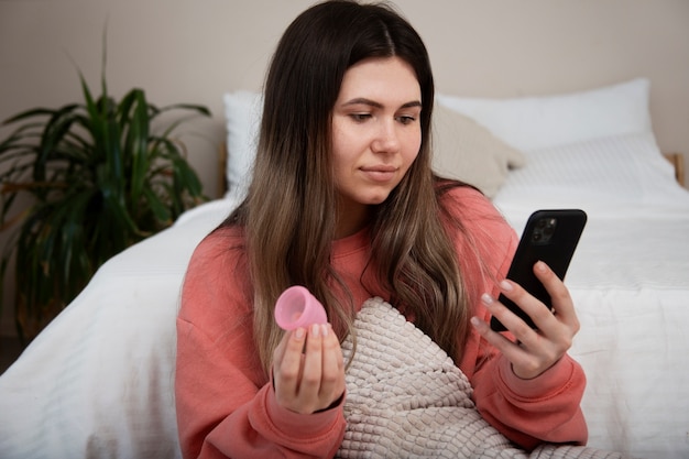 Mulher segurando copo menstrual e telefone de tiro médio