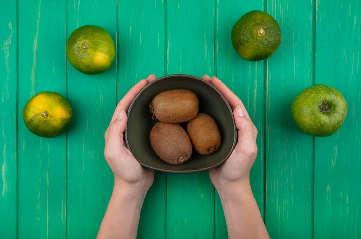Foto grátis mulher segurando kiwi em uma tigela com tangerinas verdes em uma parede verde
