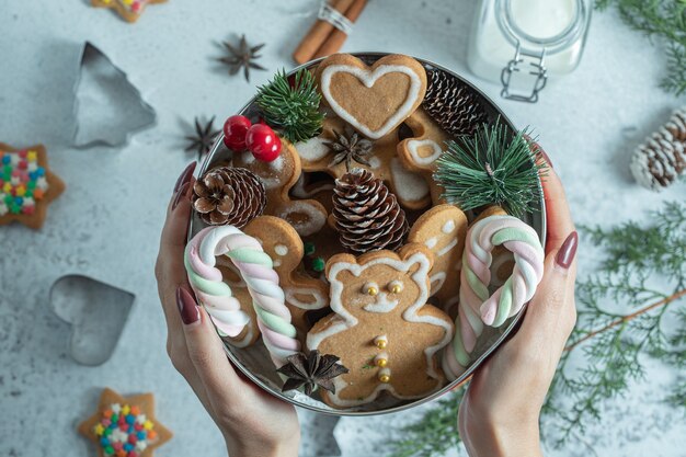 Mulher segurando louças por lado. Louça cheia de biscoitos e decorações de Natal.