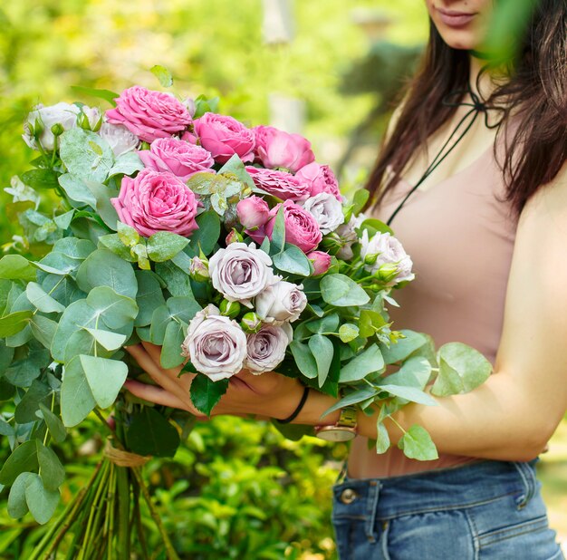 Mulher segurando o buquê de rosas cor de rosa com folhas de eucalipto no jardim