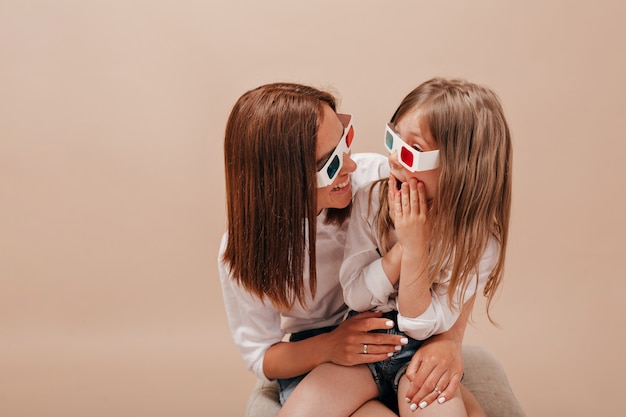 Mulher segurando sua garotinha encantadora e usando óculos para cinema. Menina assistindo filme com a mãe