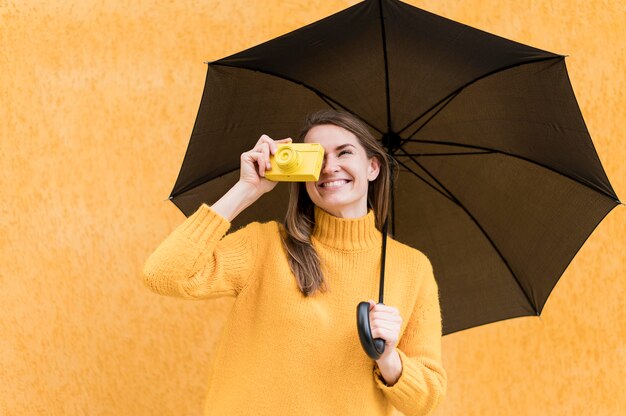 Mulher segurando um guarda-chuva preto e uma câmera amarela
