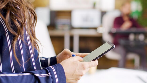 Mulher segurando um telefone nas mãos no fundo do escritório.