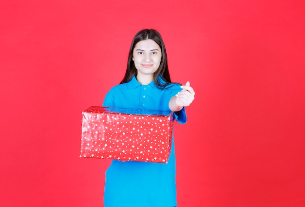 mulher segurando uma caixa de presente vermelha com pontos brancos e pedindo pagamento.