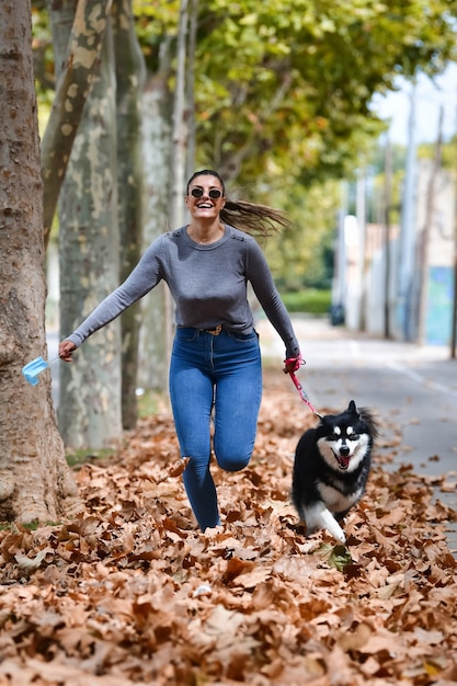 Foto grátis mulher segurando uma máscara cirúrgica e um lindo cachorro correndo em folhas secas na rua.