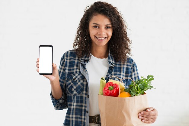 Mulher segurando uma sacola de legumes e um telefone simulado