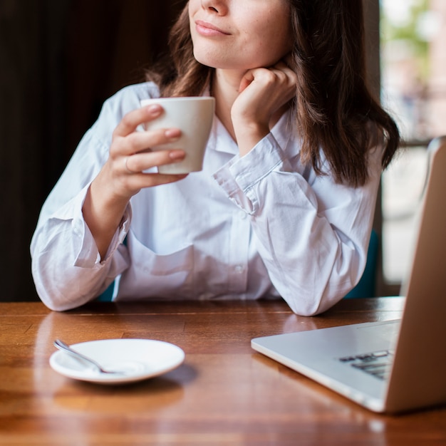 Foto grátis mulher segurando uma xícara de café com o laptop na mesa