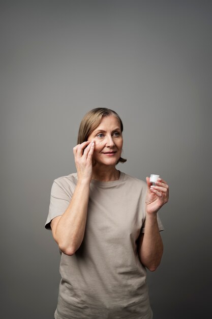 Mulher sênior de tiro médio usando creme para o rosto