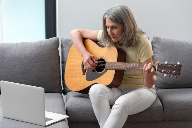 Mulher sênior em casa no sofá usando laptop para aulas de violão