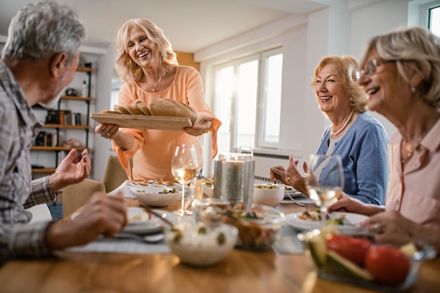 Mulher sênior feliz servindo pão para seus amigos durante a hora do almoço em casa