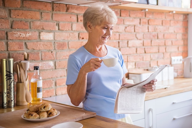 Mulher sênior lendo jornal na cozinha