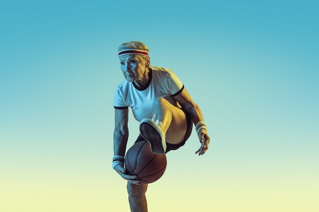 Mulher sênior no sportwear jogando basquete em fundo gradiente, luz de néon. modelo feminino em ótima forma permanece ativo. conceito de esporte, atividade, movimento, bem-estar, confiança. copyspace. Foto gratuita