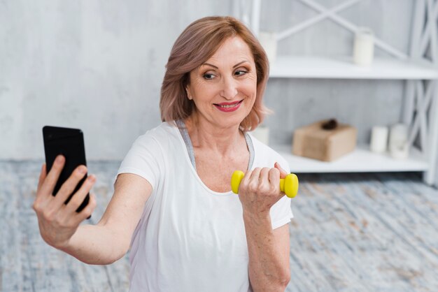 Mulher sênior, tendo selfie com halteres na mão