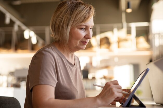 Mulher sênior trabalhando em seu tablet em um café