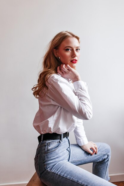 Mulher sensual em jeans olhando para a câmera Foto de estúdio da magnífica garota loira de camisa branca
