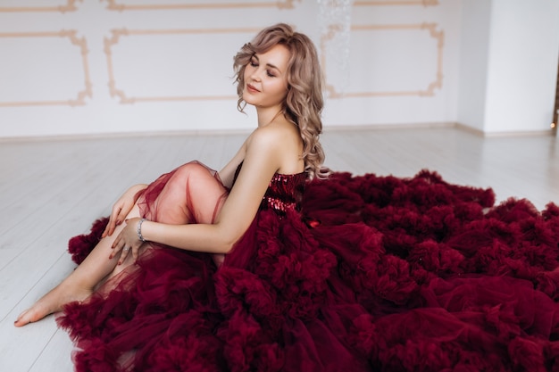 Mulher sensual em vestido vermelho burgundi encontra-se no chão na sala luminosa