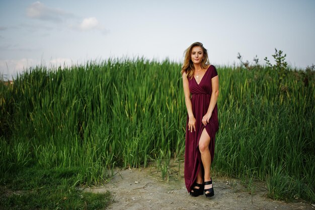 Mulher sensual loira de vestido vermelho marsala posando nos juncos