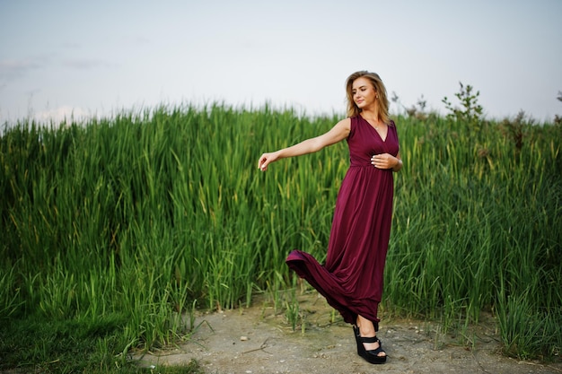 Mulher sensual loira de vestido vermelho marsala posando nos juncos