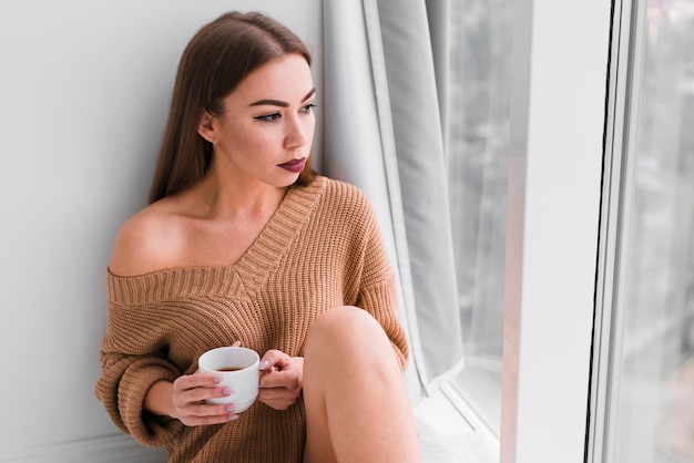 Foto grátis mulher sentada ao lado das janelas e tomando café